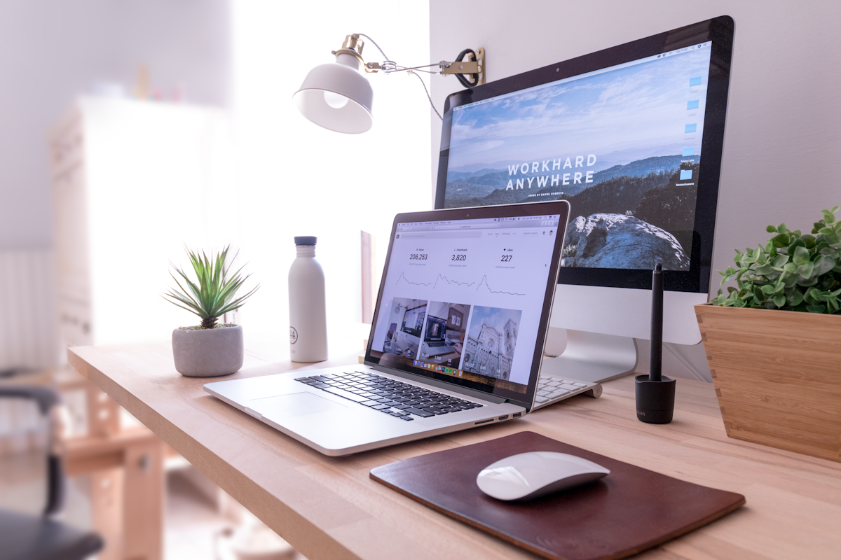 Tidy desk with a laptop, monitor, lamp, and potted plant