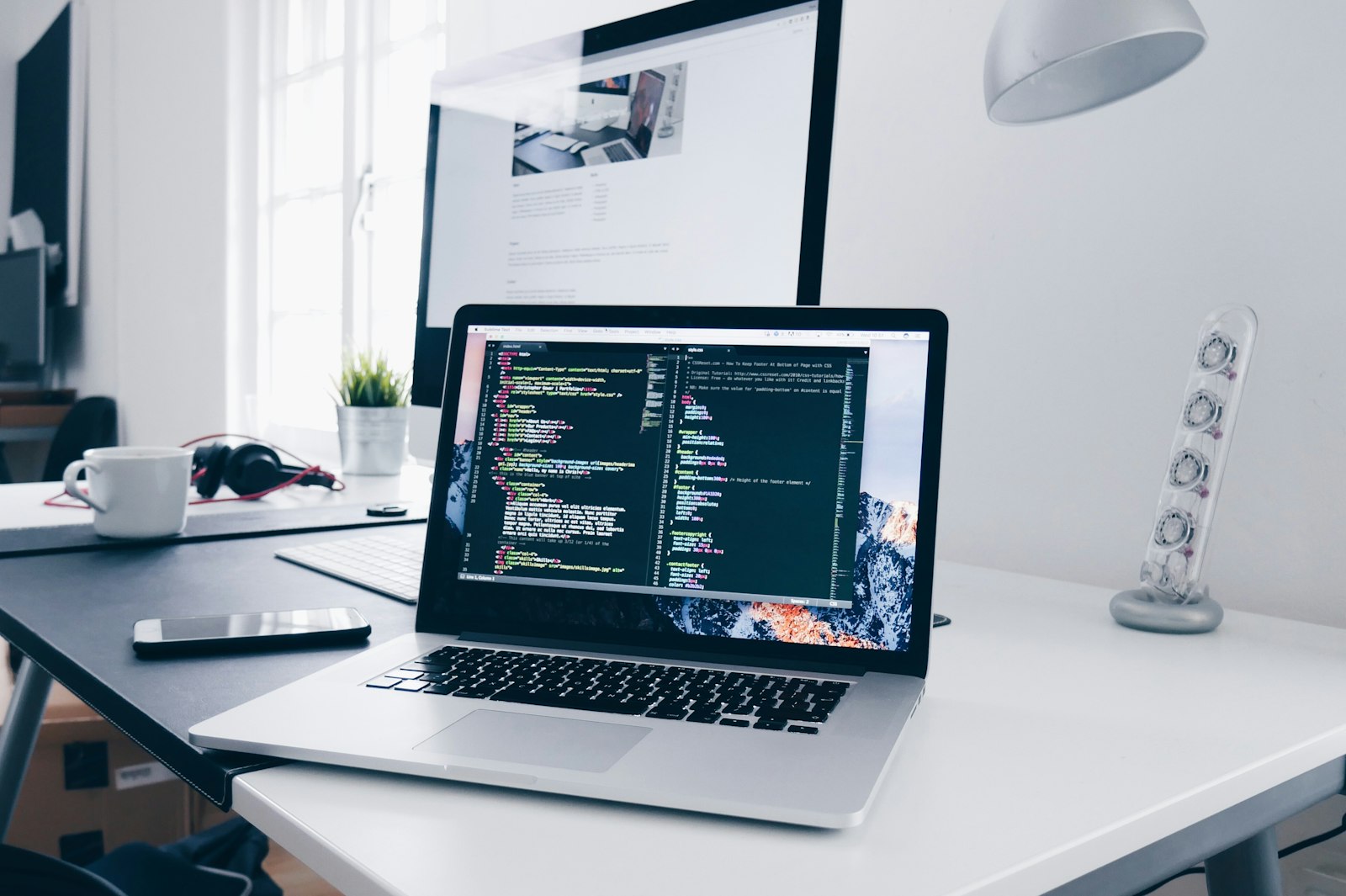 Workstation with source code open on a laptop in front of a large monitor
