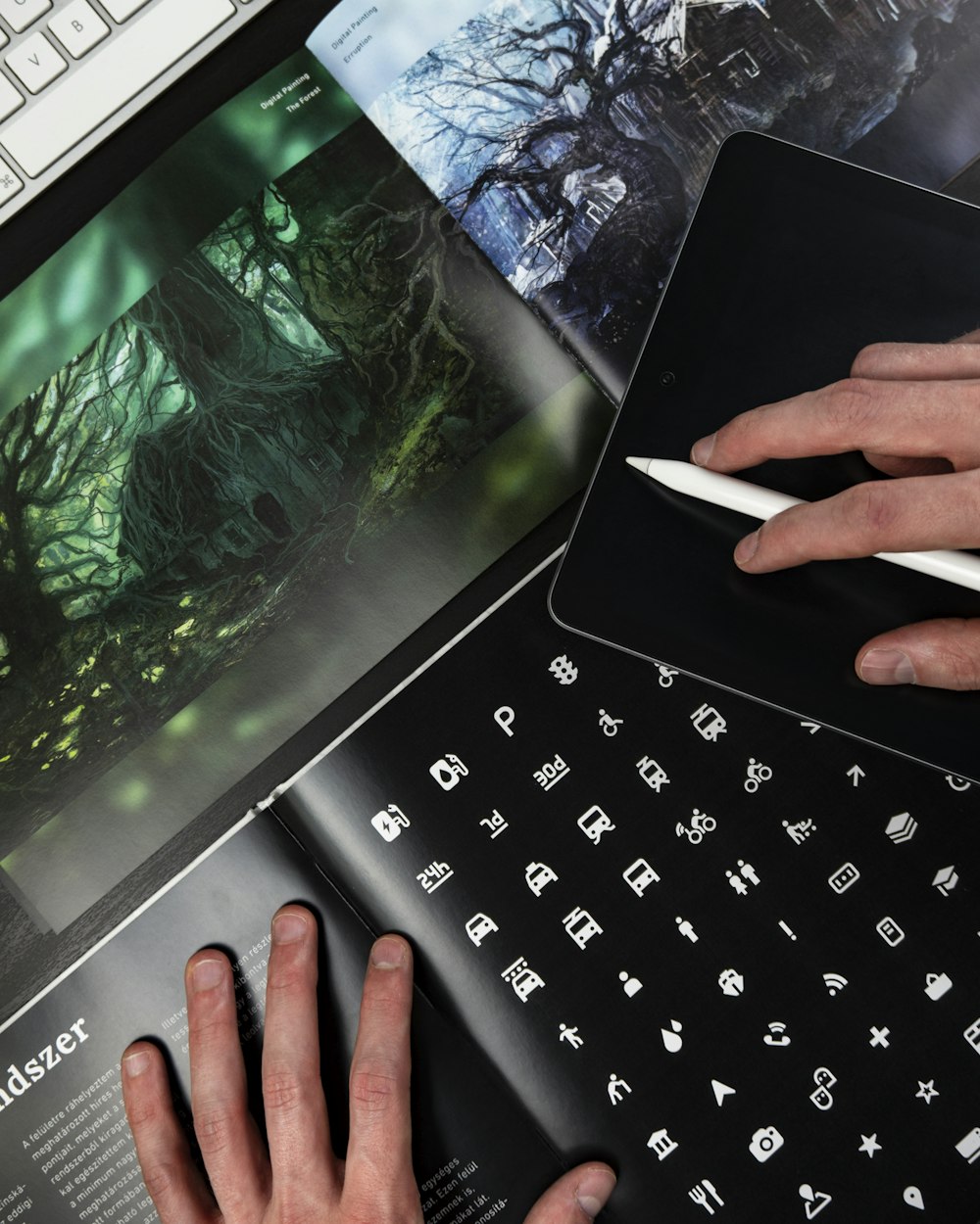 Hands sketching on a tablet with a stylus beside printed design proofs